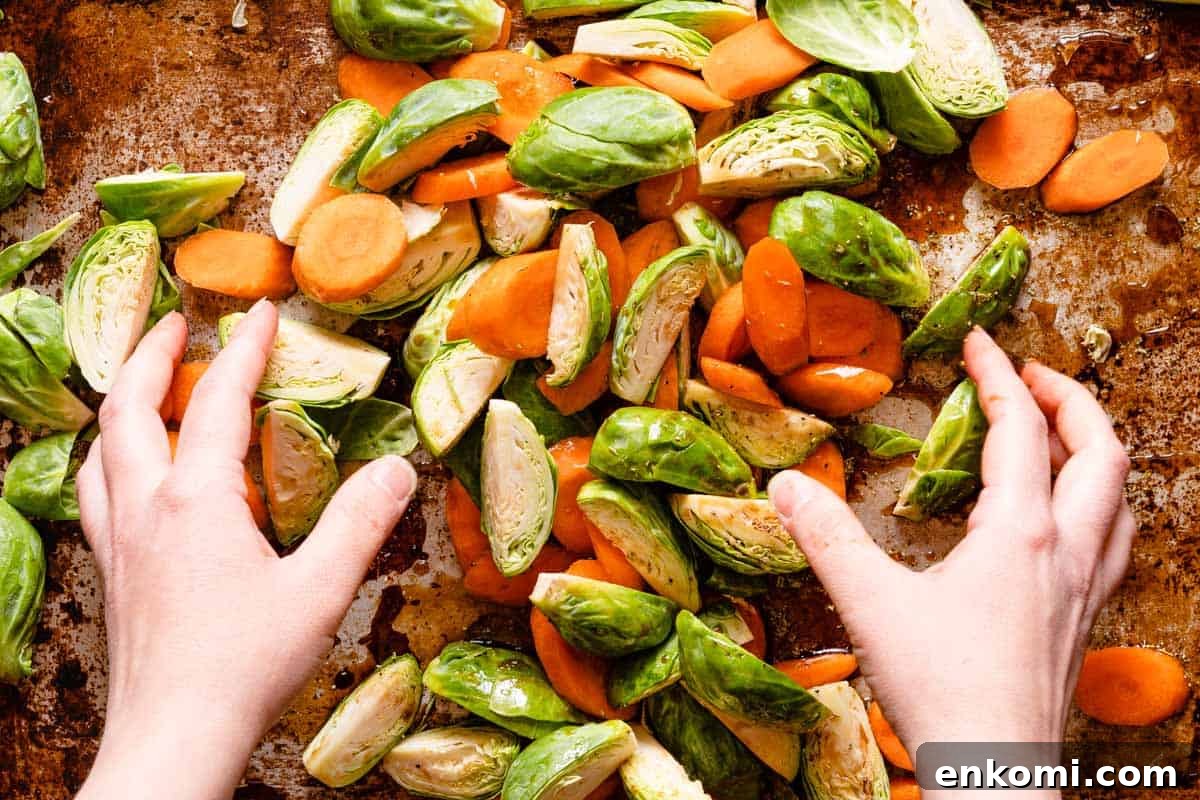 brussels sprouts and carrots being tossed with dressing on pan