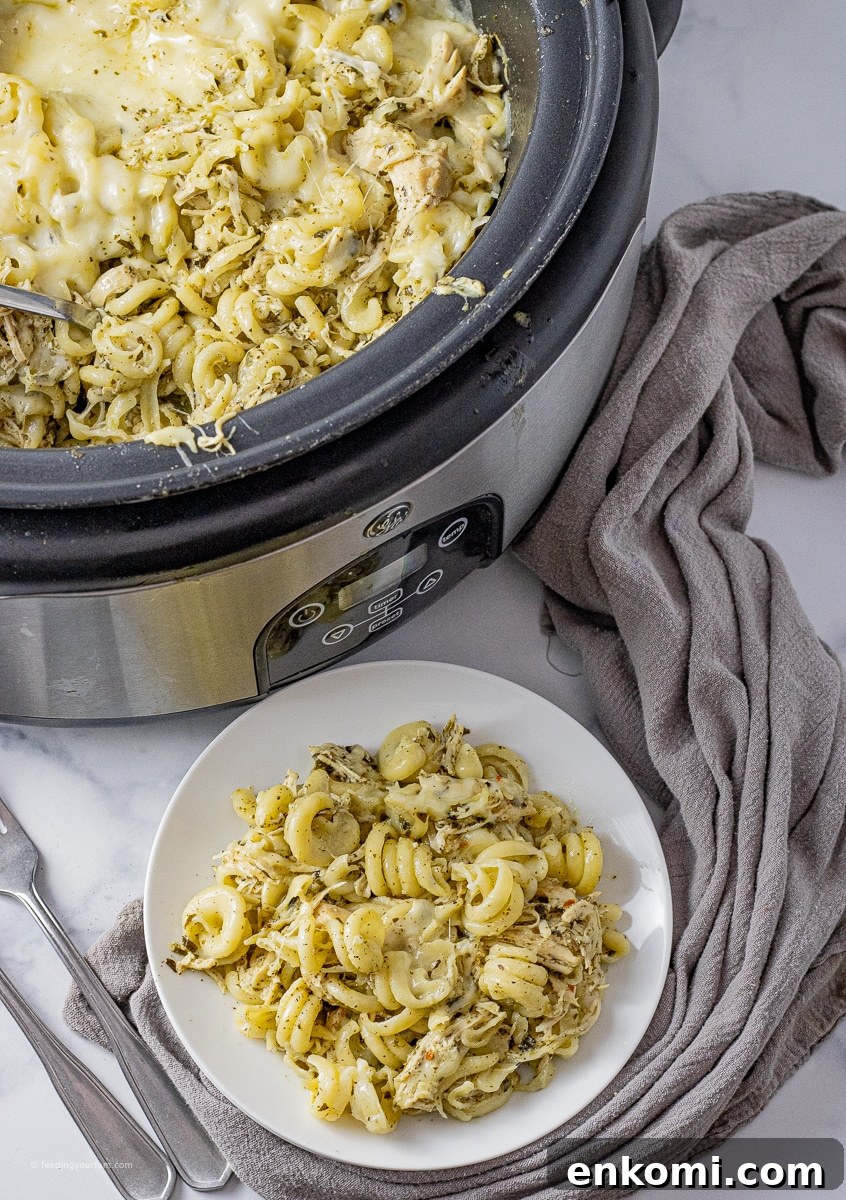 Slow Cooker Pesto Chicken Recipe for Tender, Flavorful Meals 2 slow cooker with twisted pasta, shredded chicken and pesto sauce on a white plate