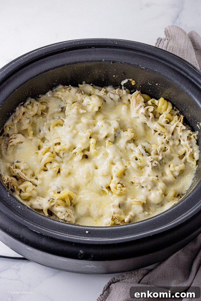 Slow Cooker Pesto Chicken Recipe for Tender, Flavorful Meals 4 Twisted noodles, pesto, shredded chicken topped with melted mozzarella cheese in a slow cooker pot