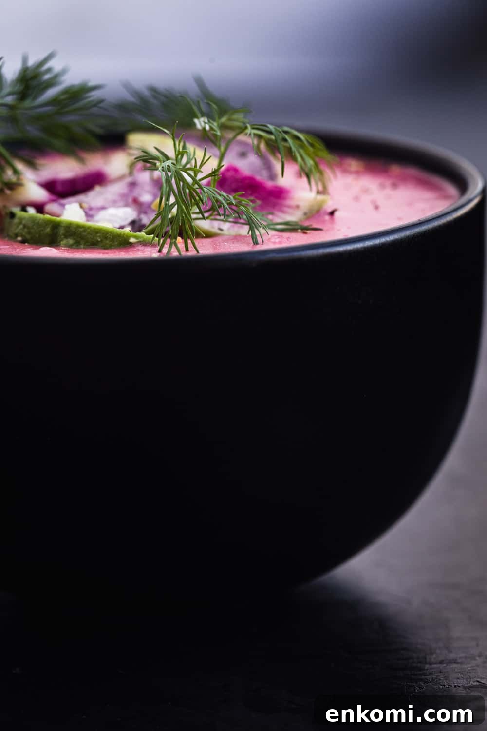 side angle shot of pink vegan potato soup with radish, avocado and dill topping.