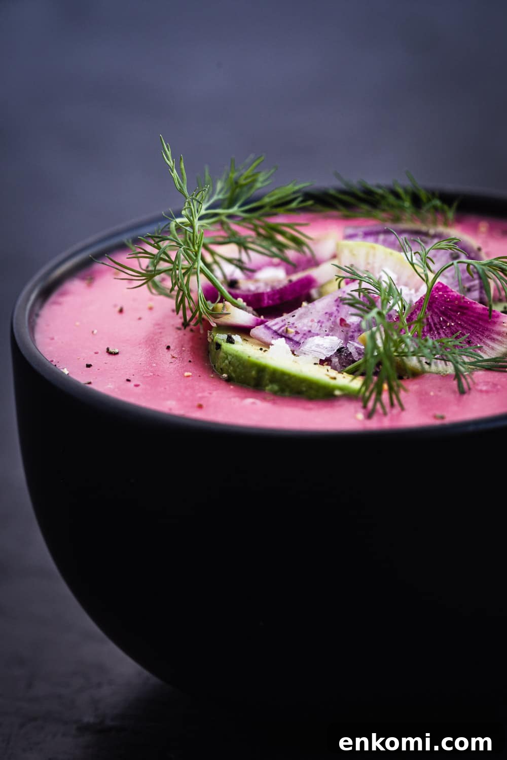 side angle shot of pink vegan potato soup with radish, avocado and dill topping.