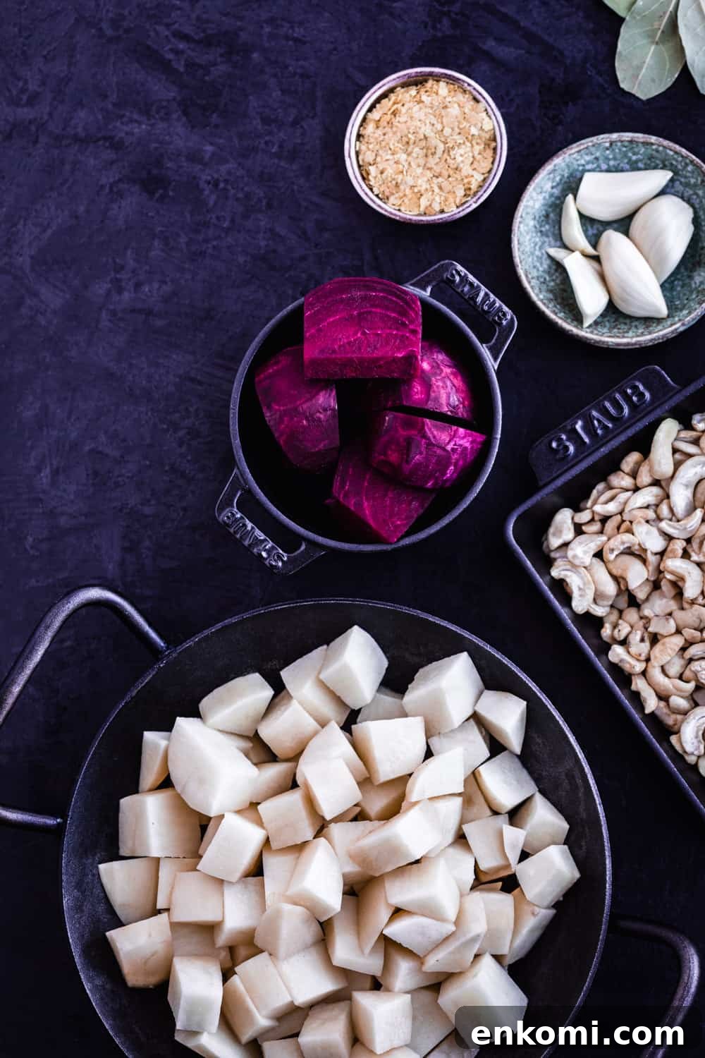 ingredient shot of vegan pink potato soup with a bowl of chopped potatoes, beets, cashews, nutritional yeast, garlic and bay leaves.