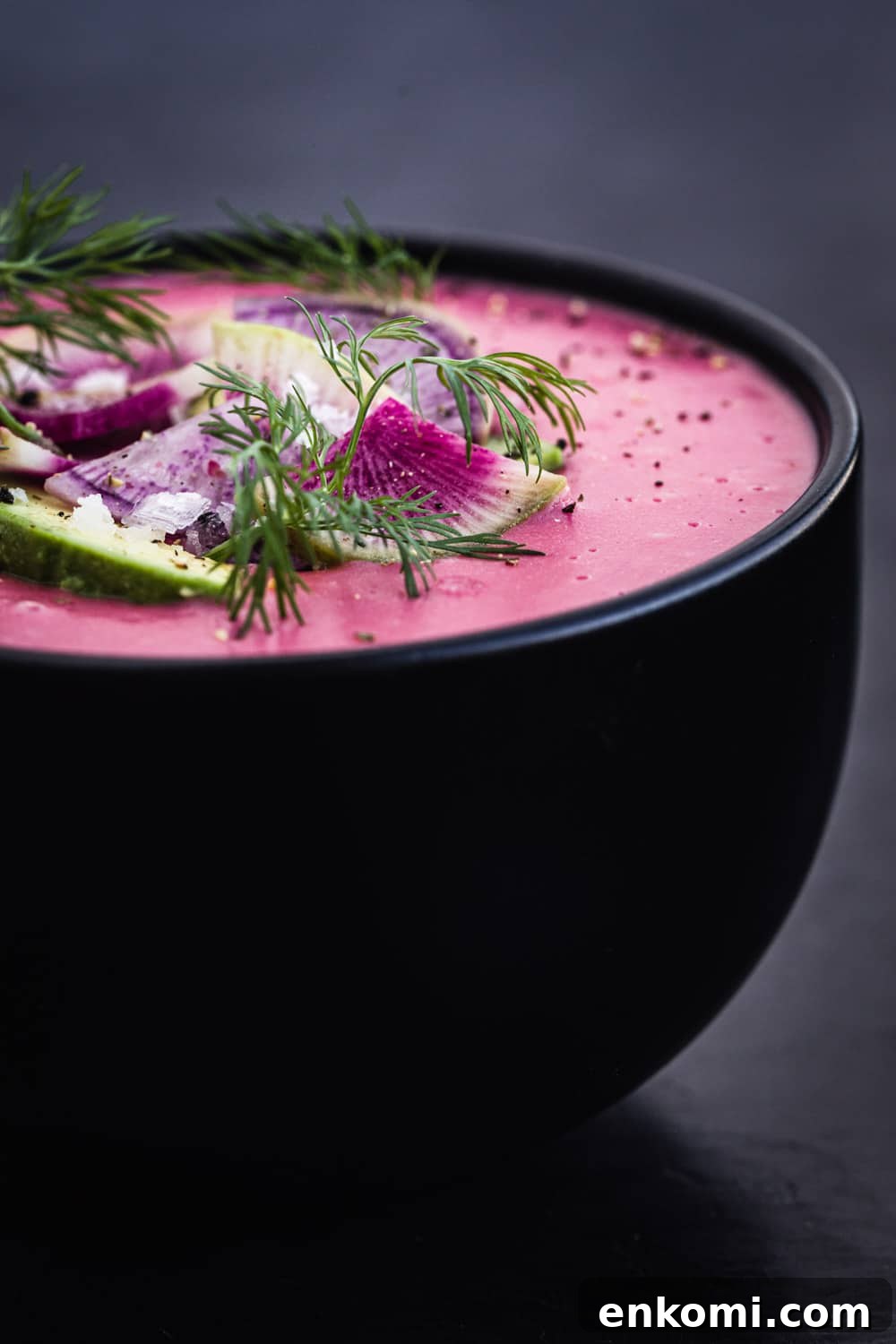side angle shot of pink vegan potato soup with radish, avocado and dill topping.