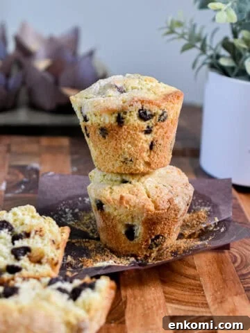 A chocolate chip muffin with self rising flour is cut in half on in front of a tower of two muffins on top of each other.