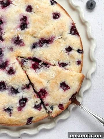 lemon blueberry sour cream cake on a cake plate with a spatula taking a piece.