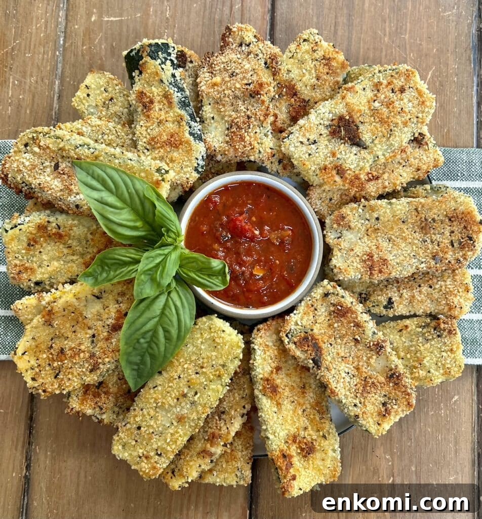 Beautiful arrangement of baked panko crusted zucchini on a round platter with a small bowl of tomato sauce in the center with basil garnish.