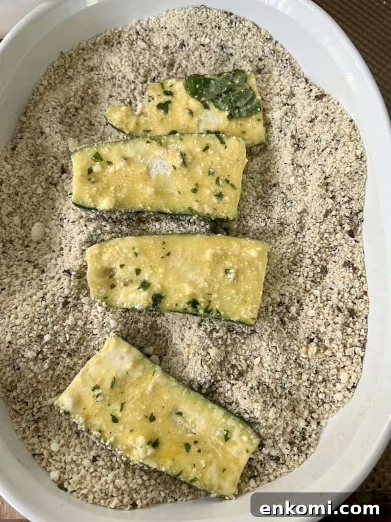 Four slices of zucchini placed in seasoned panko breadcrumbs after being dipped in egg mixture.
