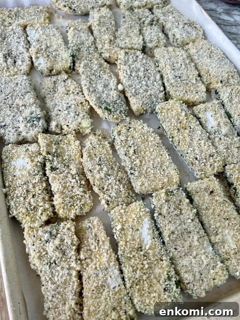 Breaded zucchini and squash sliced arranged on parchment lined and rimmed sheet pan.
