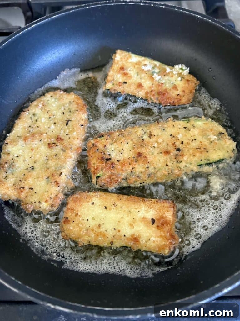Frying four breaded zucchini slices in oil in pan.