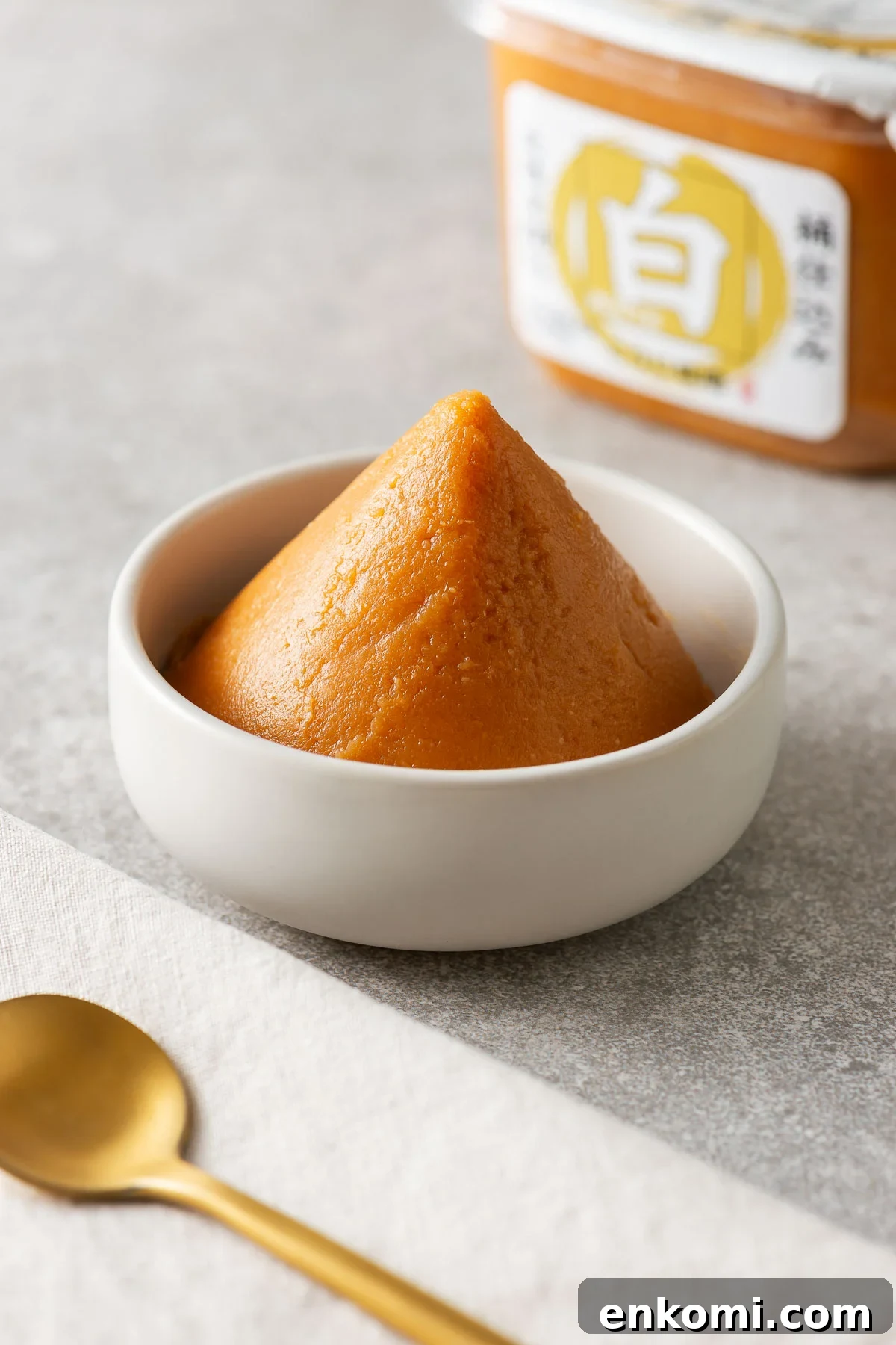 Miso Substitutes and Alternatives: What to Use — and What to Avoid 2 Whit miso paste shaped into a triangle in a small white bowl next to a tub of white miso paste.