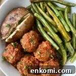 overhead shot of cooked meatballs, green beans, and a baked potato in a white plate