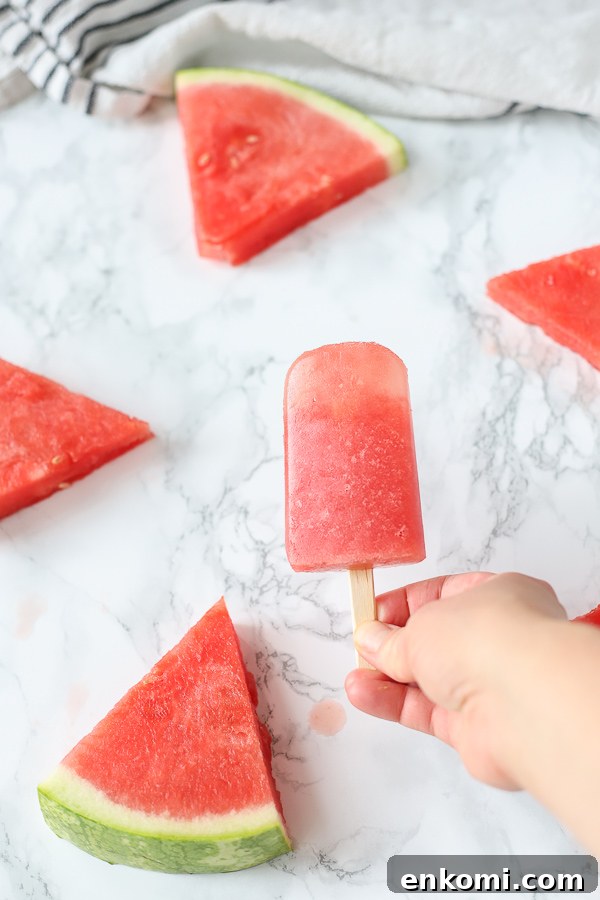 hand holding watermelon popsicles with watermelon in the backgrond