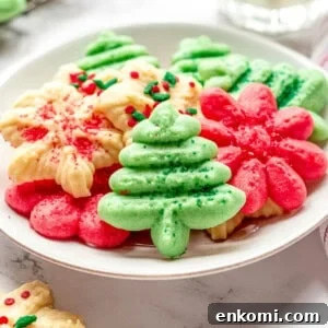 A plate of cream cheese spritz cookies in the shape of Christmas trees, flowers, and snowflakes.