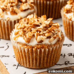 A carrot cake muffin with cream cheese glaze topped with pecans.