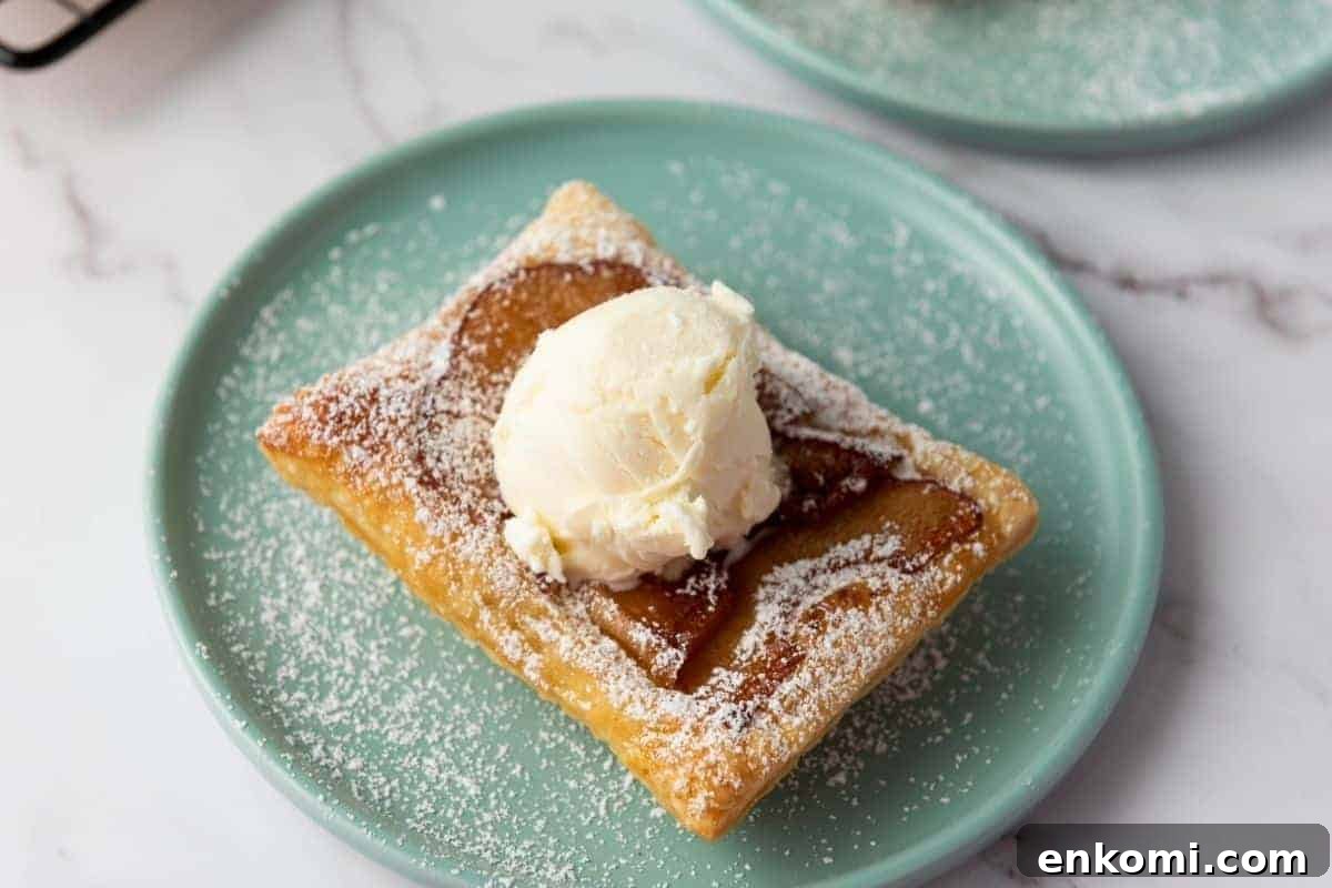 29 Fall Desserts That Bring Generations of Flavor Together 2 A Puff Pastry Apple Tart topped with a scoop of vanilla ice cream and sprinkled with powdered sugar sits on a light green plate.