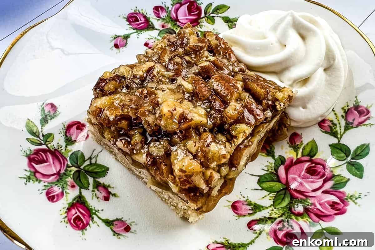 29 Fall Desserts That Bring Generations of Flavor Together 15 A slice of maple pecan pie bar topped with chopped pecans on a floral-patterned plate.