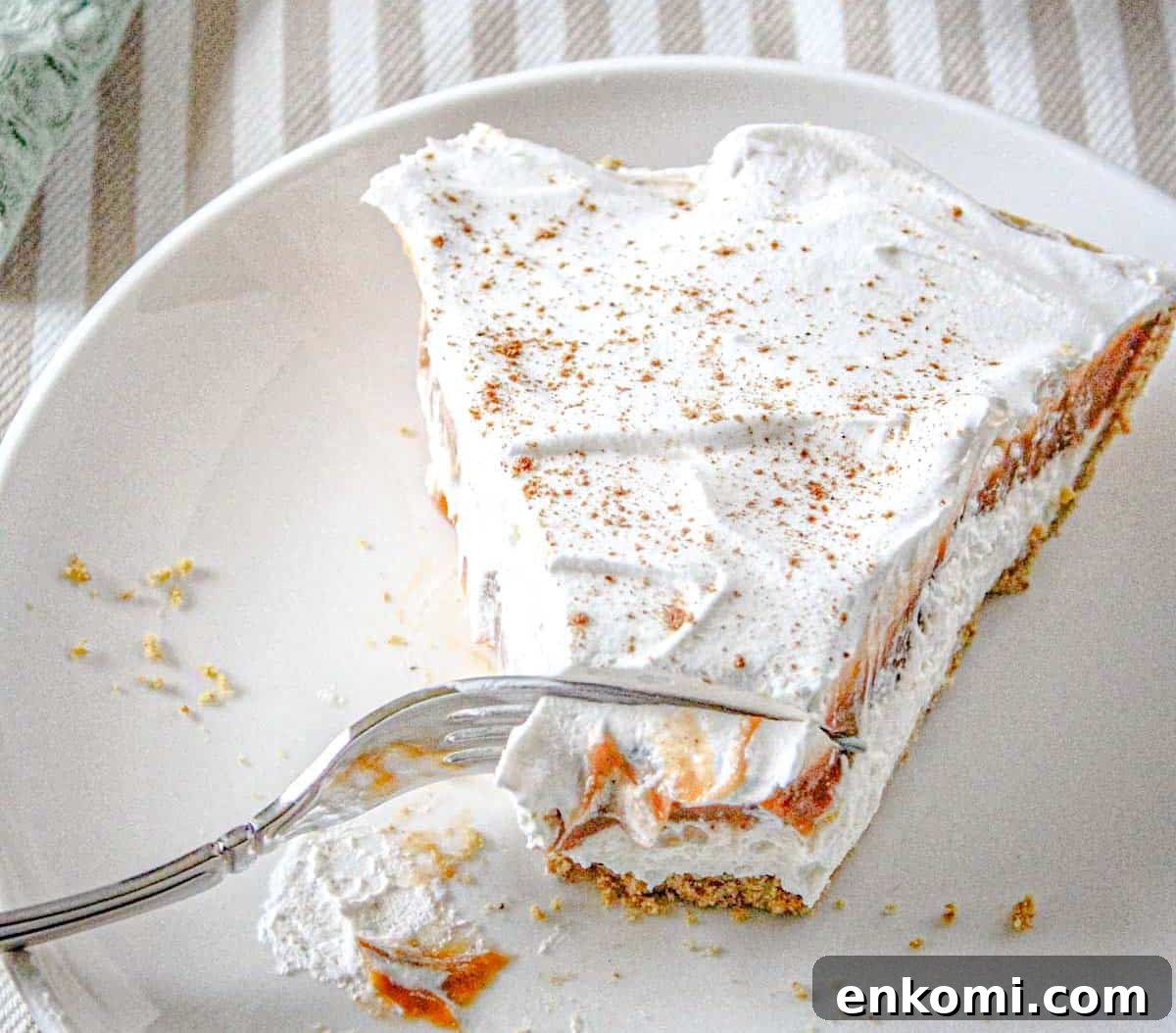 29 Fall Desserts That Bring Generations of Flavor Together 8 A slice of no-bake pumpkin cheesecake on a white plate, partially eaten with a fork resting on the plate.
