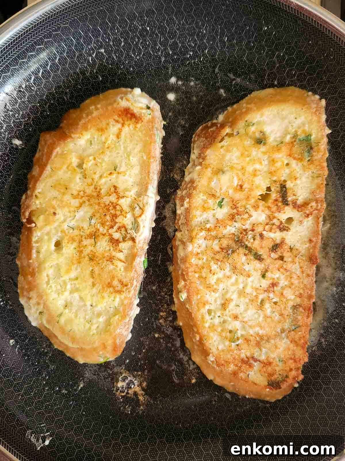 Parmesan, Lemon & Herb Savory French Toast Recipe 9 Two slices of French toast in a pan being showing the browned cooked side.