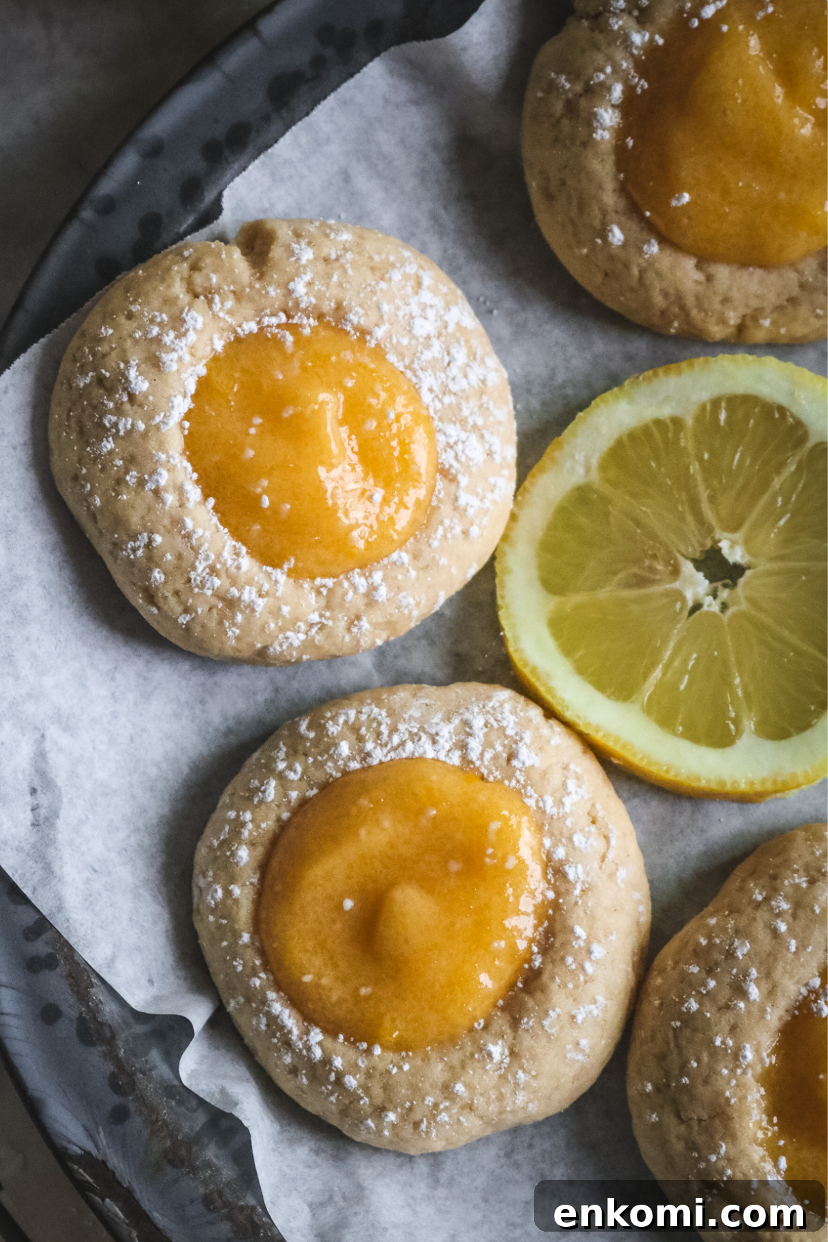 overhead view of chewy lemon curd thumbprint cookies on a gray pie plate lined with parchment paper.