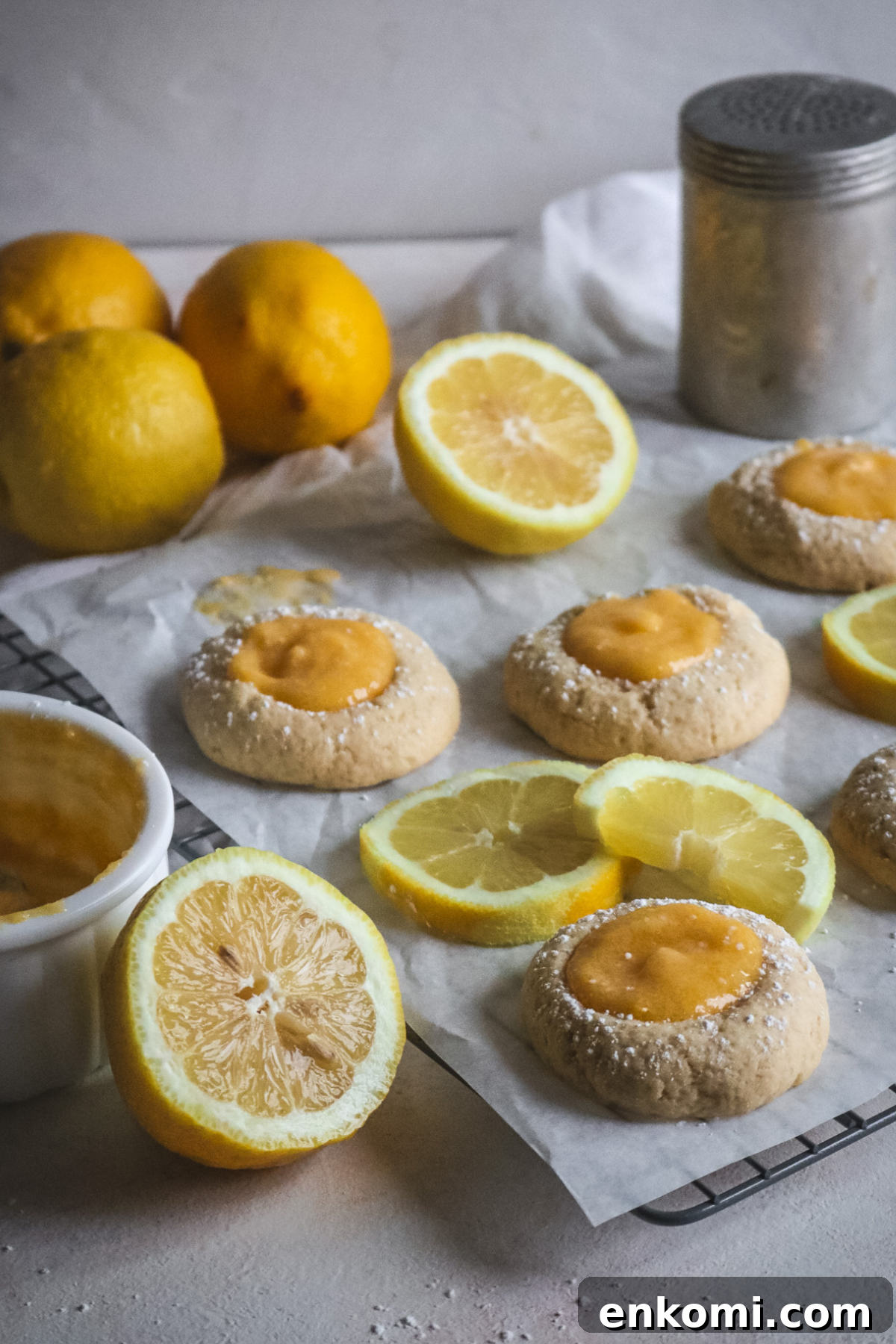 wire rack with parchment paper and fresh lemon curd thumbprint cookies next to sliced lemons.