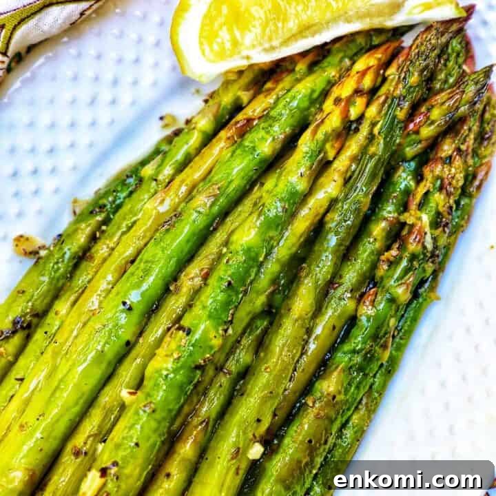 white serving plate with grilled asparagus, garlic, and lemon wedge.