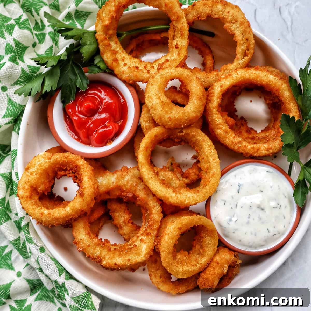 bowl of air fryer onion rings with sides of ranch dressing and ketchup..