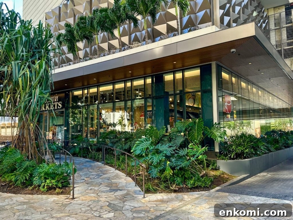 Exterior of Island Country Markets at Ritz-Carlton Residences, Waikīkī. The building features tropical greenery, floor-to-ceiling windows, and modern design.