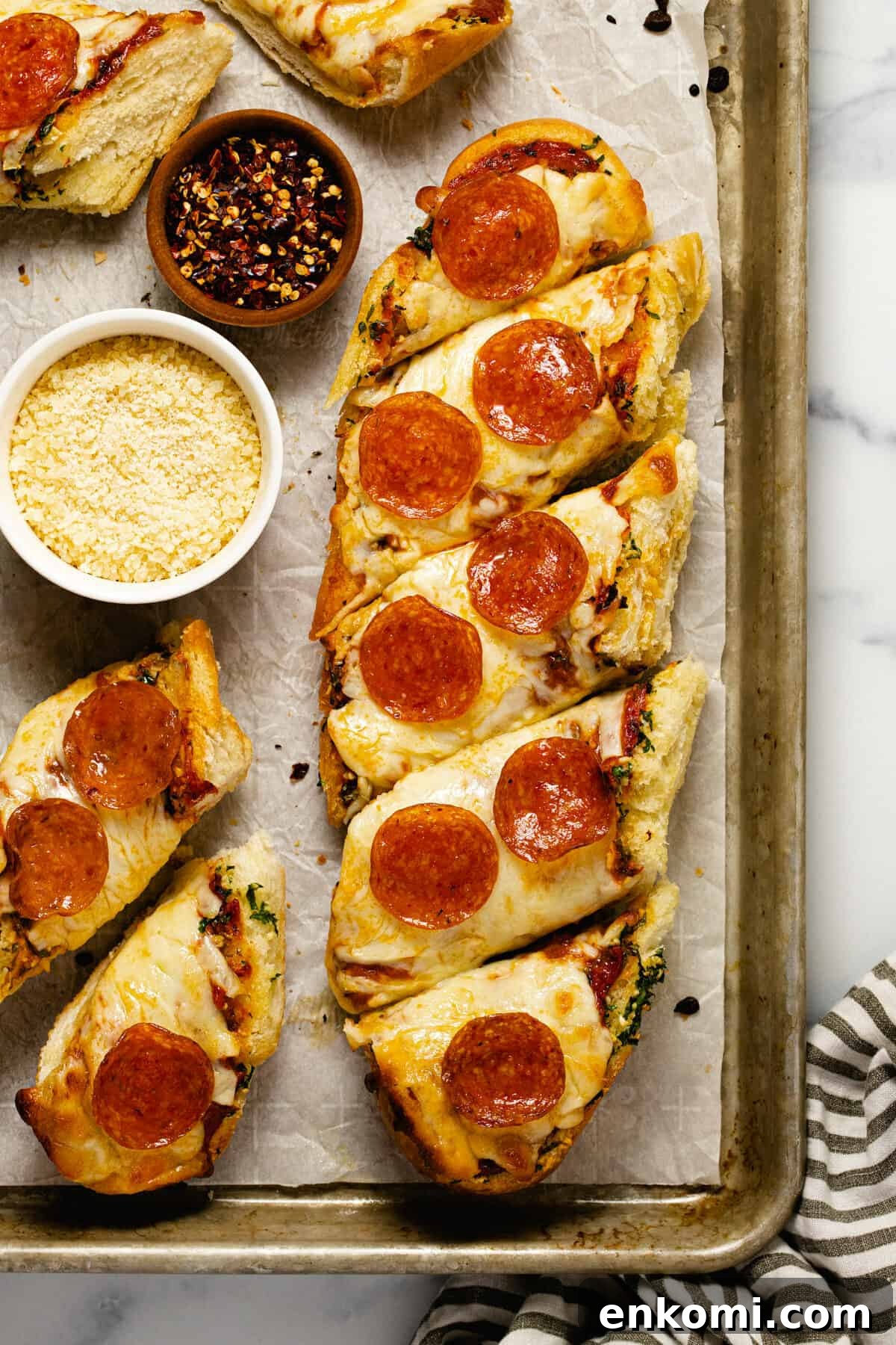 Baking sheet with homemade garlic bread pizza and a small bowl of grated Parmesan cheese