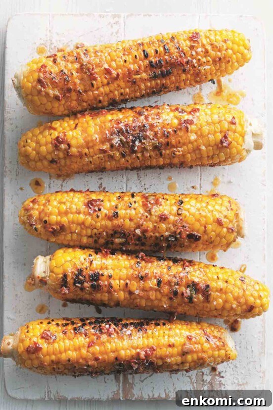 Five ears of grilled corn on the cob with chipotle butter on a white wooden board.