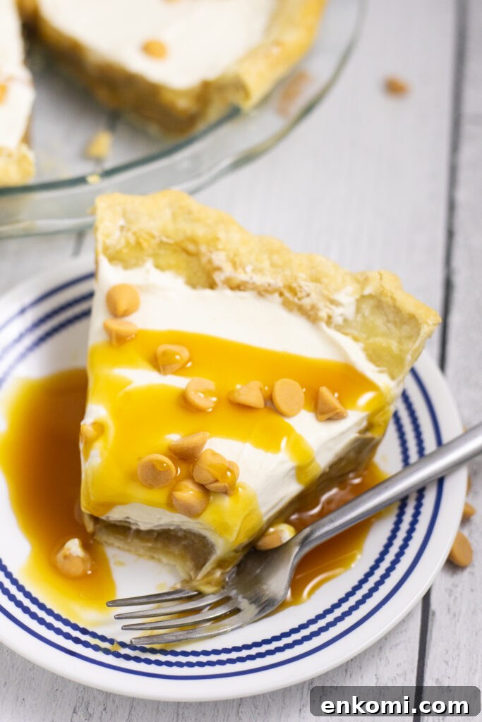 Classic Butterscotch Pie Recipe with Creamy Caramel Filling 2 Overhead view of a slice of butterscotch pie on a small plate with a fork and a bite missing. The pie is drizzled with butterscotch sauce and topped with butterscotch chips.
