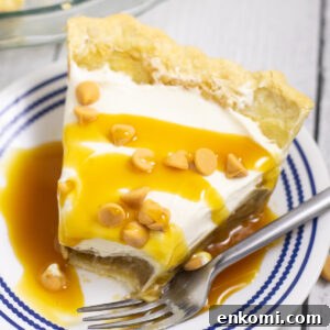 Overhead view of a slice of butterscotch pie on a small plate with a fork and a bite missing. The pie is drizzled with butterscotch sauce and topped with butterscotch chips.