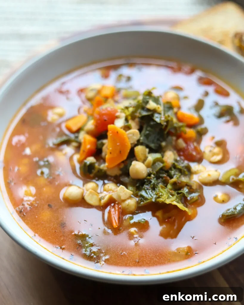 close up view of a bowl of vegan sausage kale soup with veggies, chickpeas, and a tomato broth.