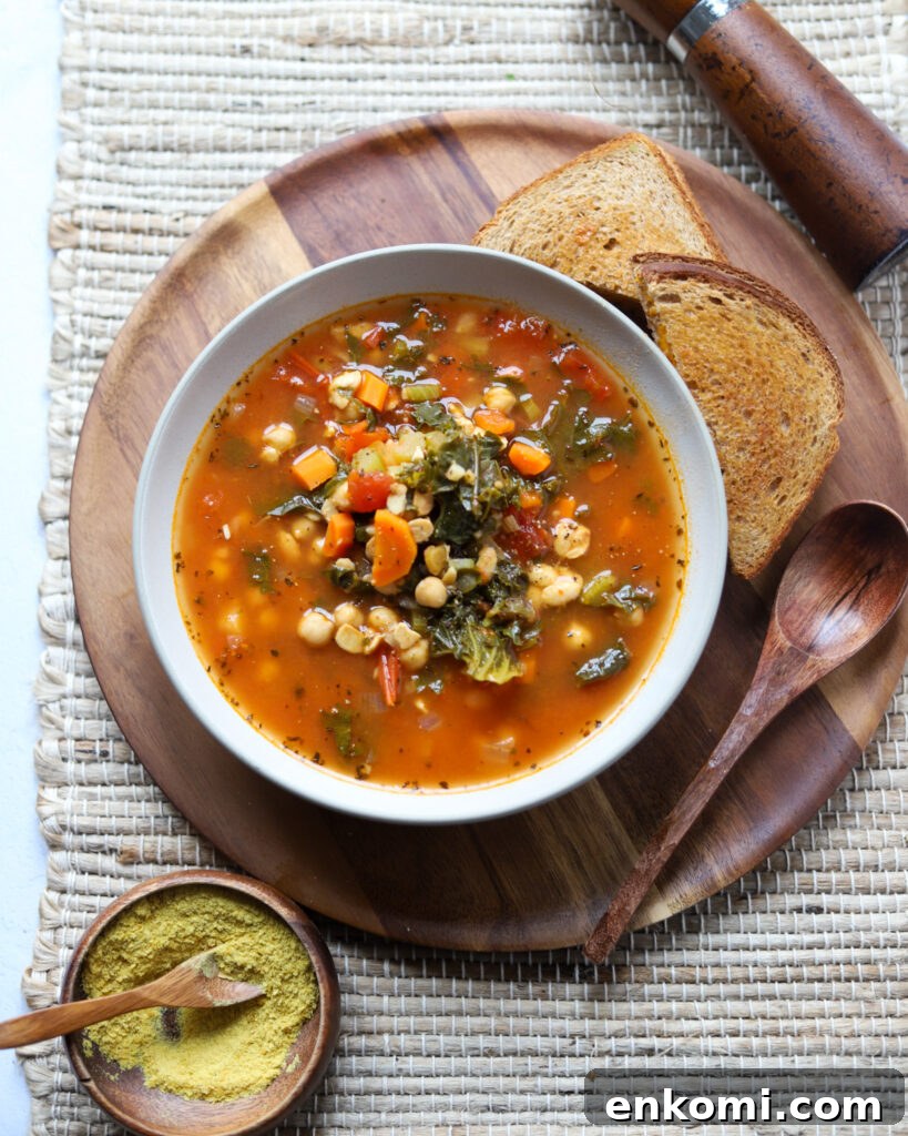 overhead view of a bowl of vegan sausage and kale soup with chickpeas and more on a wooden plate with toast.