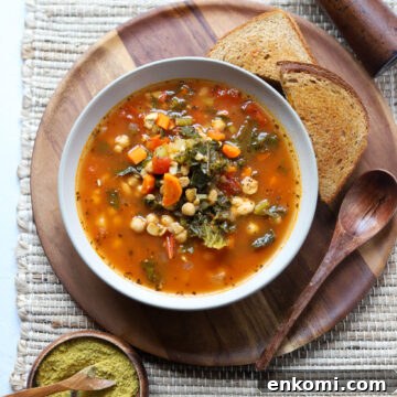 overhead view of a white bowl with vegan sausage kale soup made with tempeh next to toast and a wooden spoon.