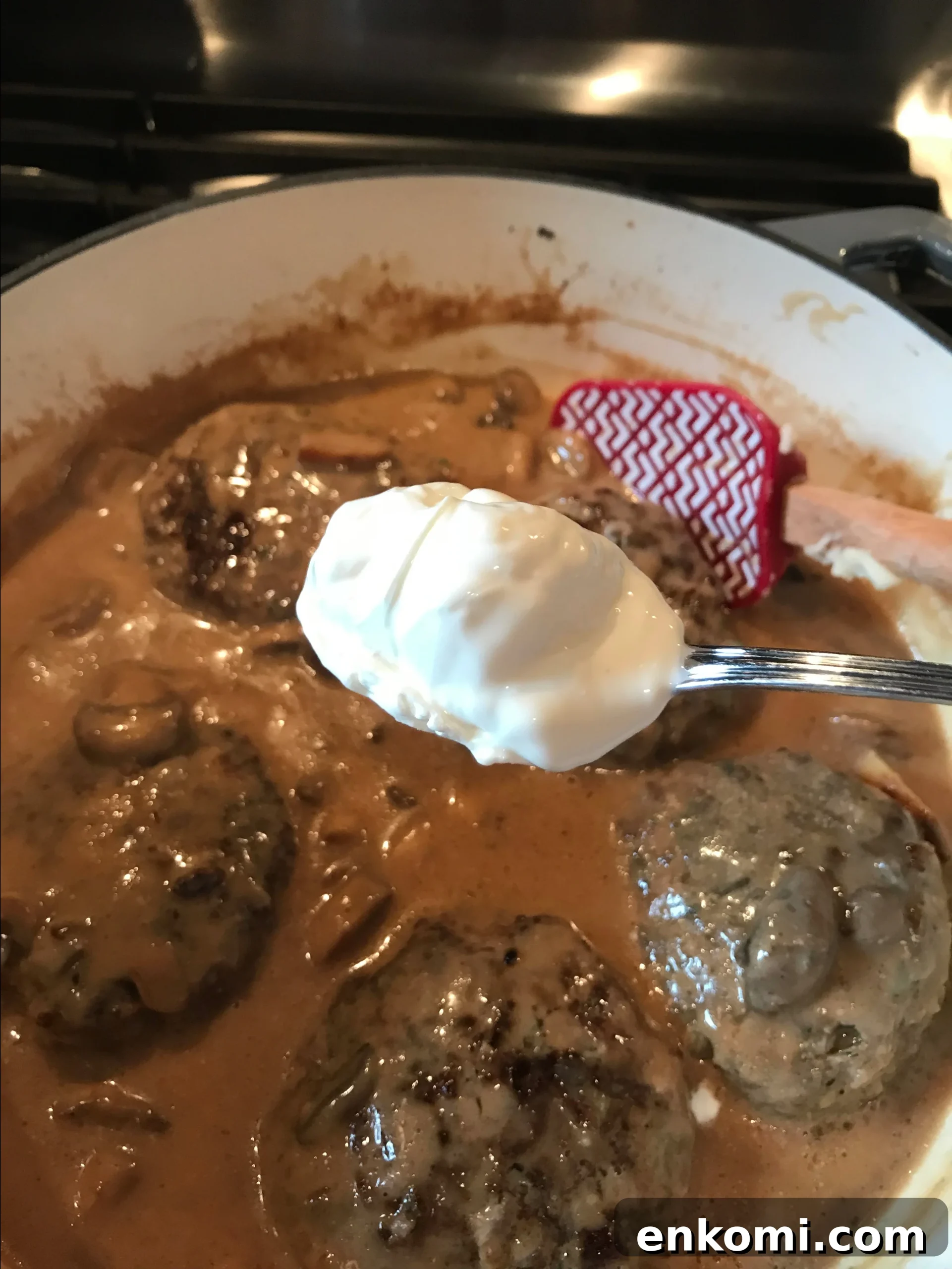 A spoon of sour cream about to be put in the cooking burgers