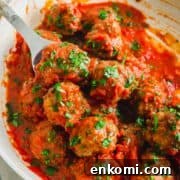 A large serving bowl filled with venison meatballs garnished with chopped parsley.