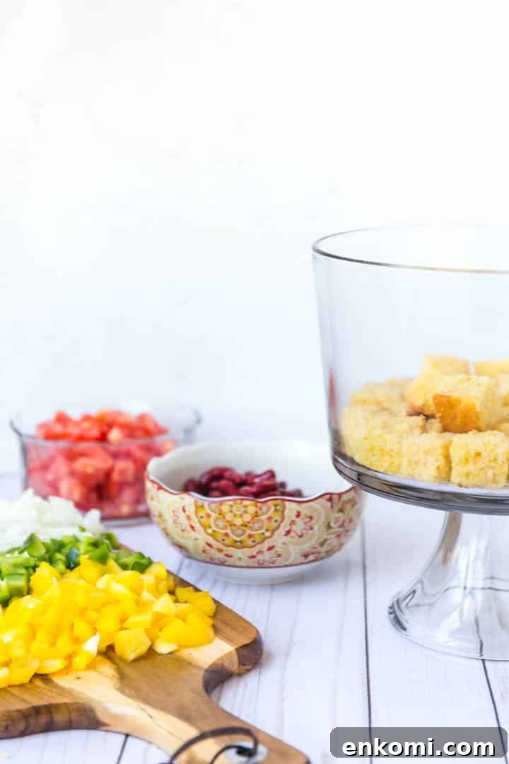 Classic Southern Cornbread Salad Recipe 5 A photo of a glass trifle bowl with cornbread in the bottom, cutting board of ingredients.