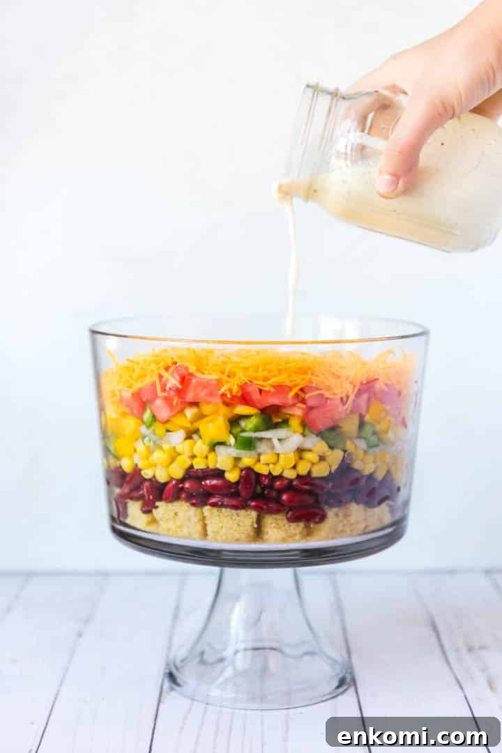Classic Southern Cornbread Salad Recipe 6 The ranch dressing being poured over the top of a colorful bowl of ingredients