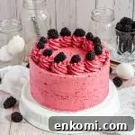 A bright pink gluten-free frosted honey blackberry cake topped with frosting swirls and fresh blackberries.