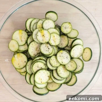 Zucchini slices in a bowl drizzled with olive oil and seasoned with salt and pepper.