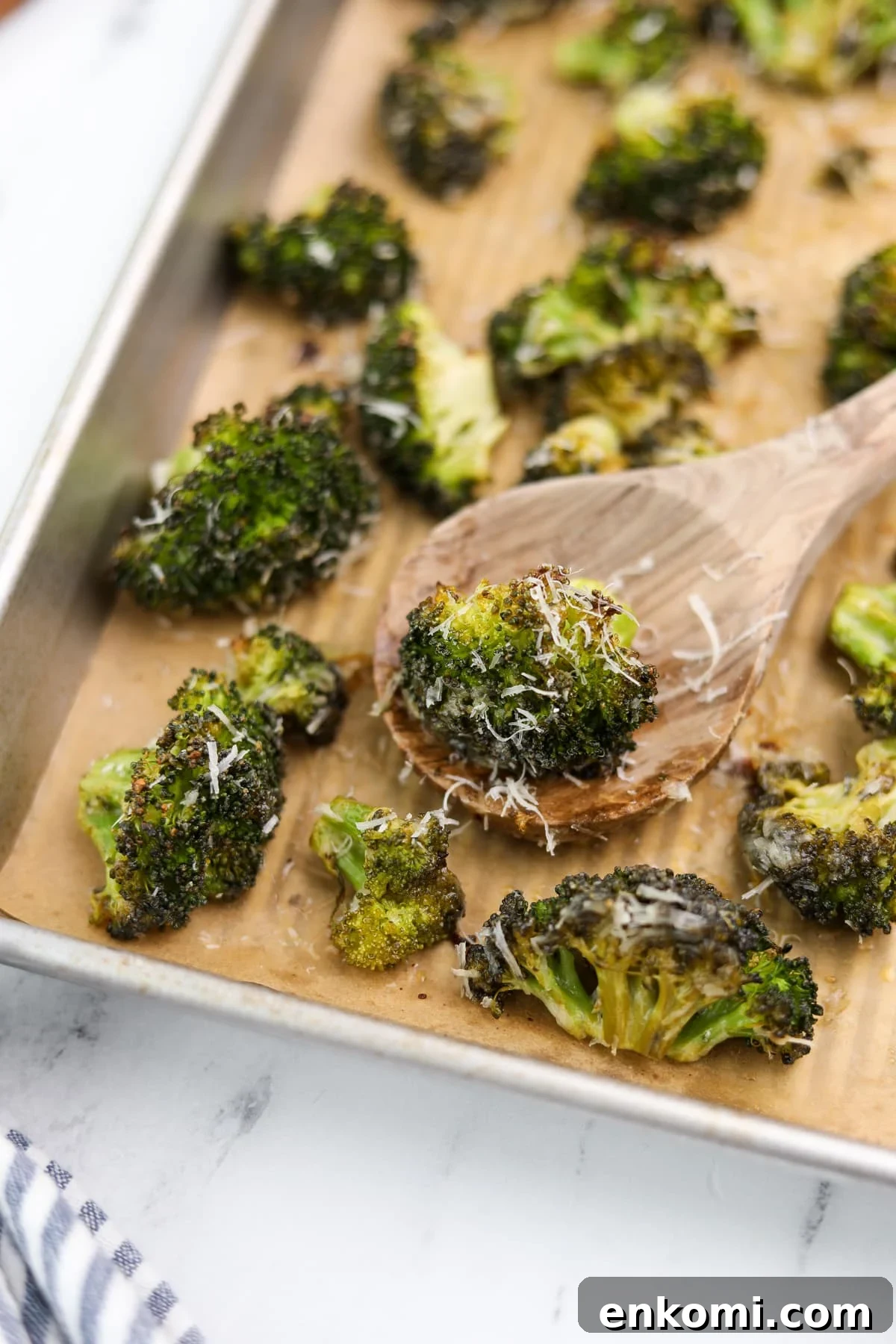 A wooden spoon taking a portion of roasted broccoli from a baking sheet.