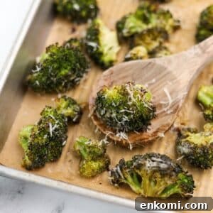 A wooden spoon taking a portion of roasted broccoli from a baking sheet.
