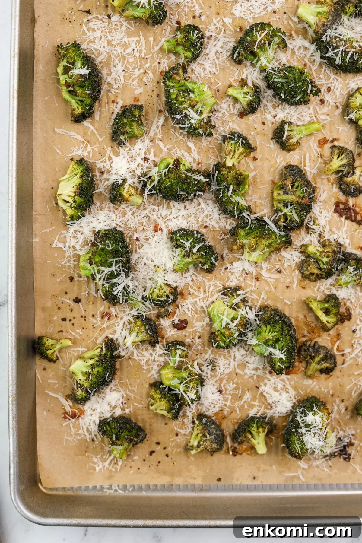 Roasted broccoli on a baking sheet topped with parmesan cheese.