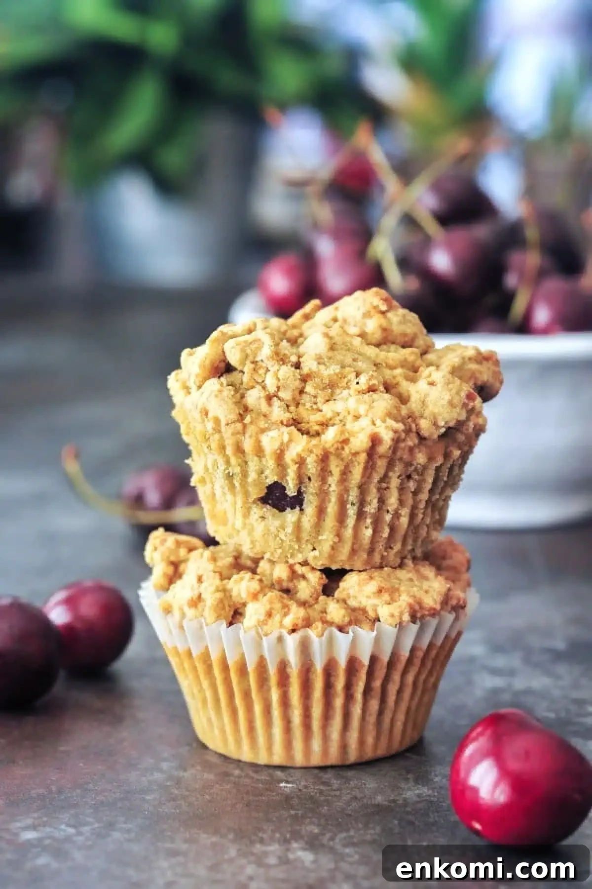 Two cherry zucchini muffins stacked one on top of another, with a bowl of fresh cherries in the background.