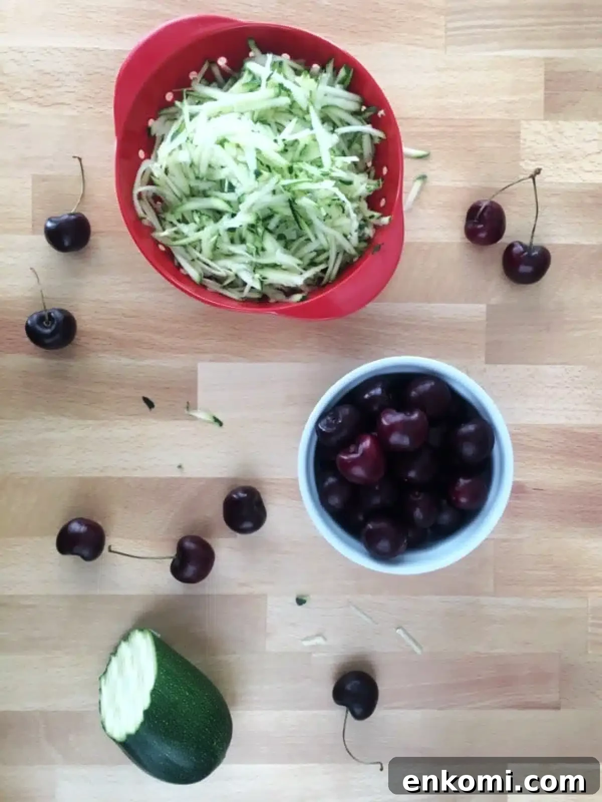 How to make cherry zucchini muffins: bowls of fresh grated zucchini and pitted cherries on a butcher block.