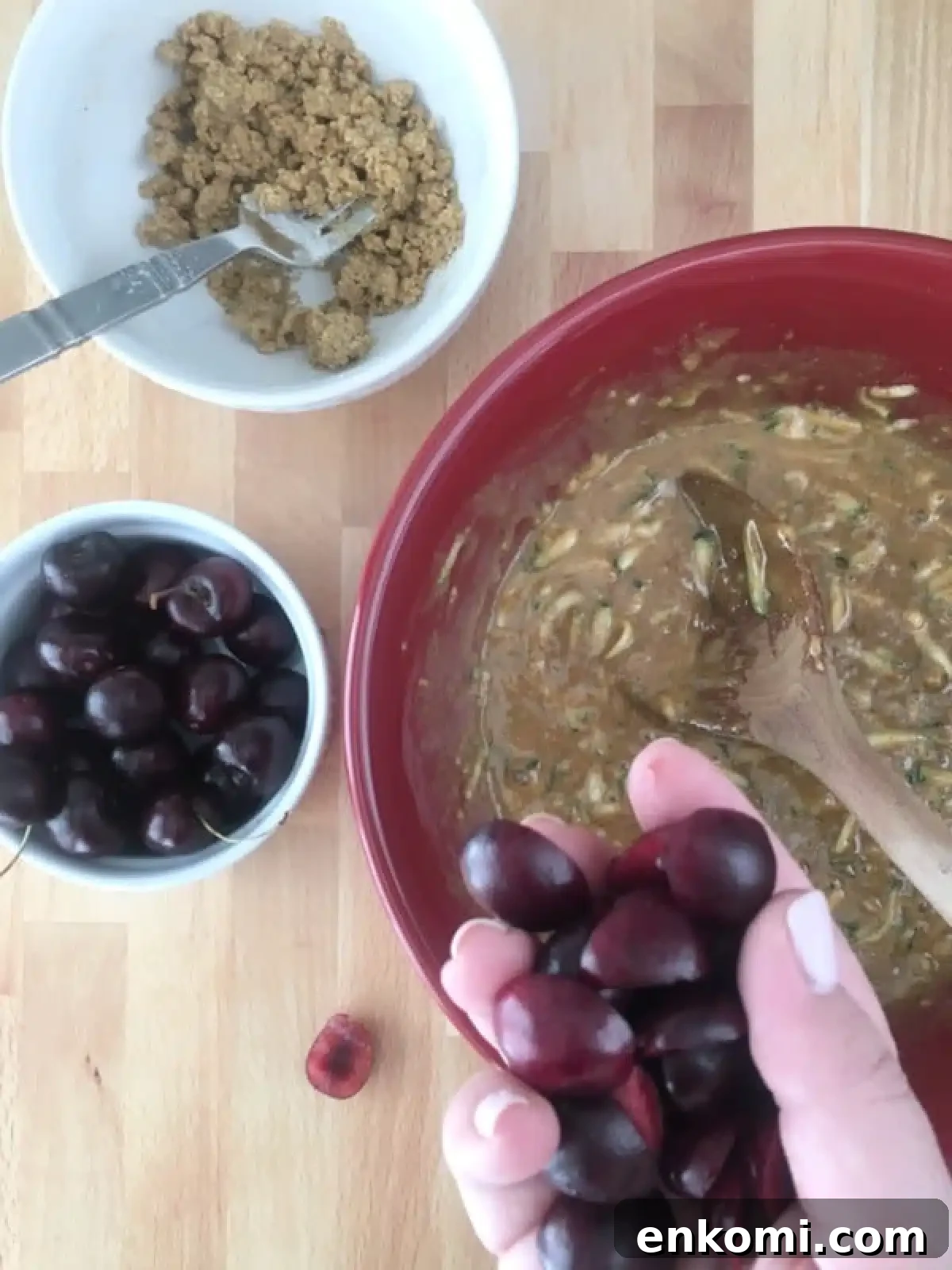 How to make cherry zucchini muffins: bowl of muffin batter, chopped cherries in a hand, crumb topping in a smaller bowl.