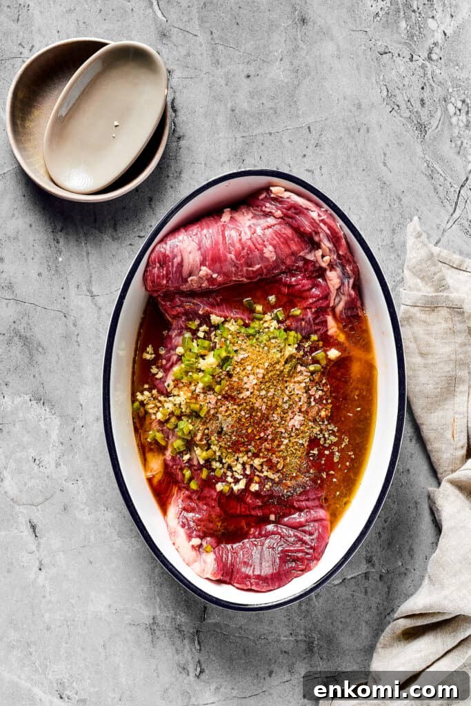 A flank steak in an enamel oval dish, covered in marinade.