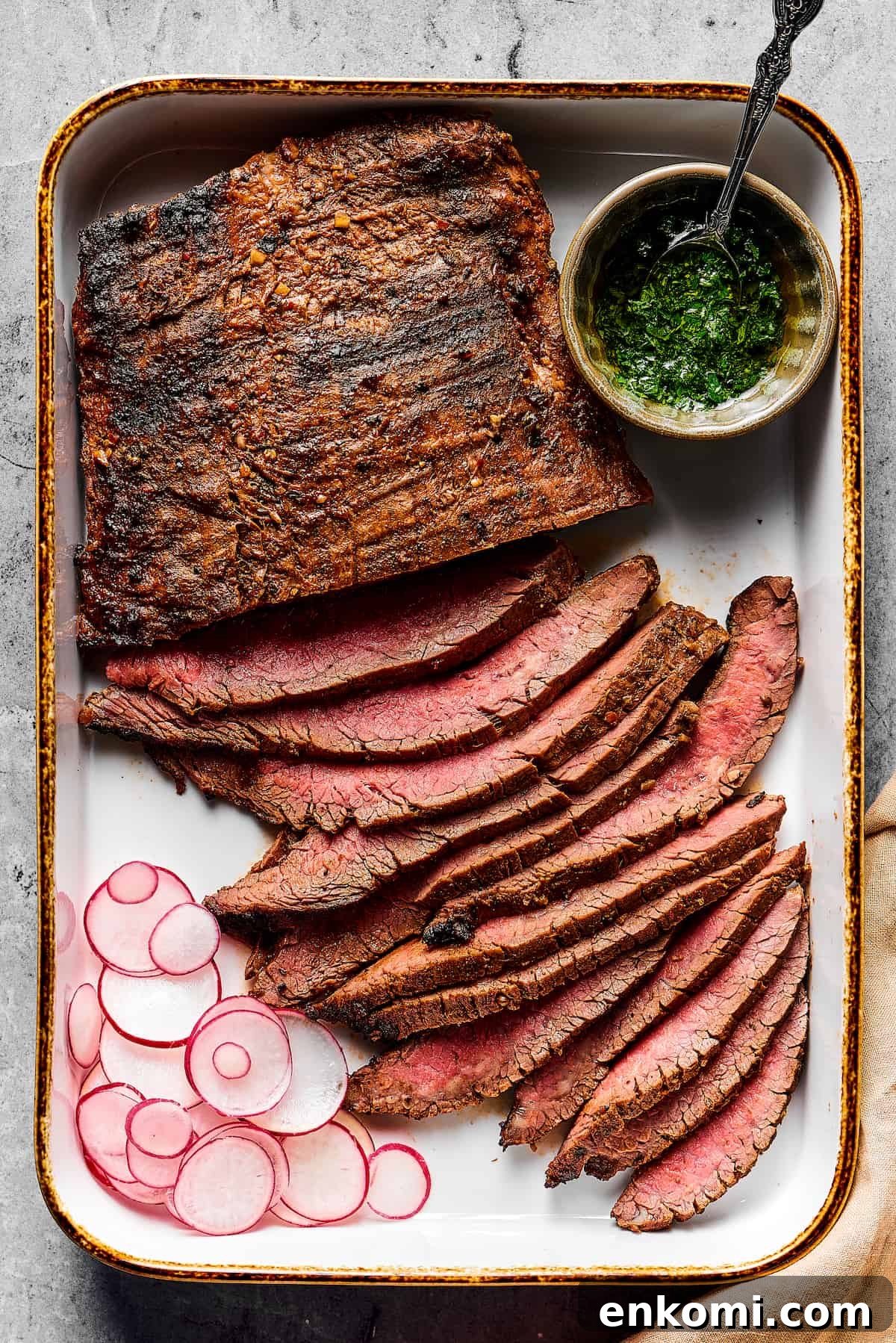 Grilled flank steak, partially sliced into thin strips, with a cup of dipping sauce on one side and a sliced radish on the other.