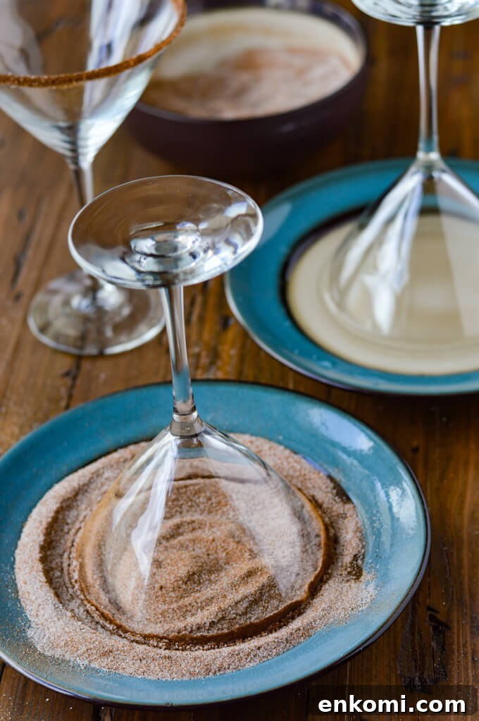 Two plates one with water and a martini glass dipped in it. Another one with pumpkin spice sugar and a martini glass dipped in it. One martini glass sitting upright with spiced sugar on its rim.