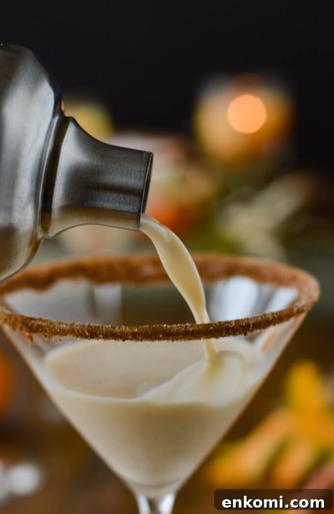 Pouring a pumpkin spice martini from a cocktail shaker into a martini glass with spiced sugar on its rim.